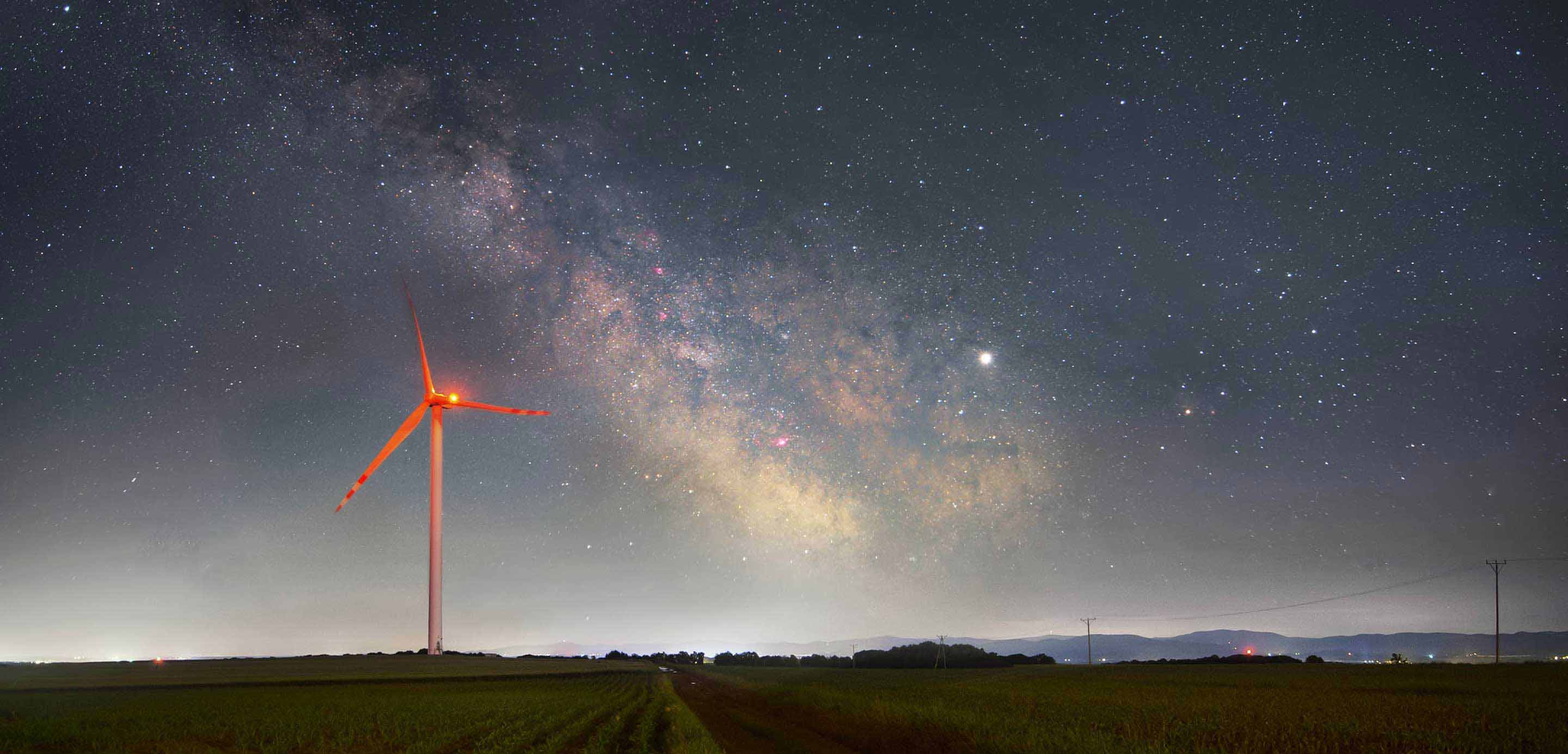 A wind turbine illuminated against the night sky, harnessing renewable energy in the darkness. 