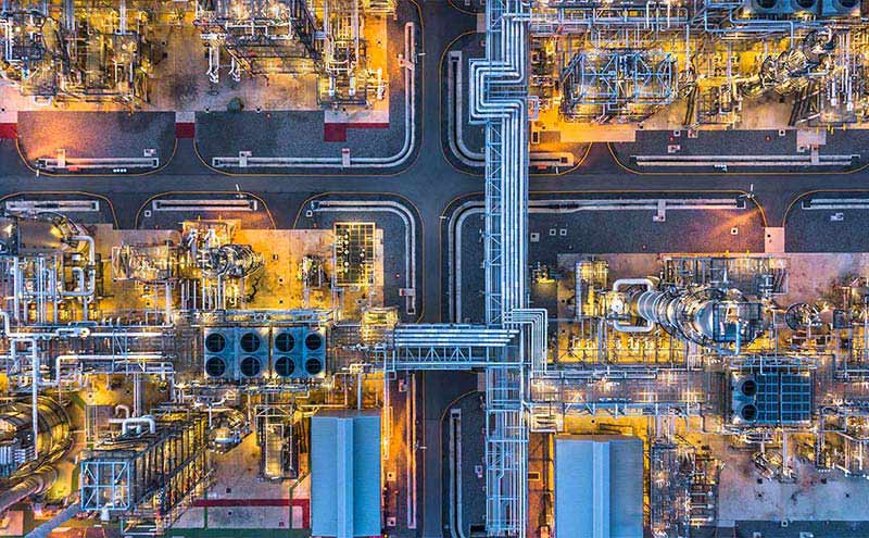 Aerial view of a refinery at night, showcasing the illuminated structures and machinery in operation. 
