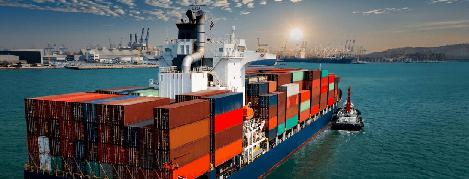 A cargo ship in a calm ocean with vibrant orange and pink hues reflecting on the water. 