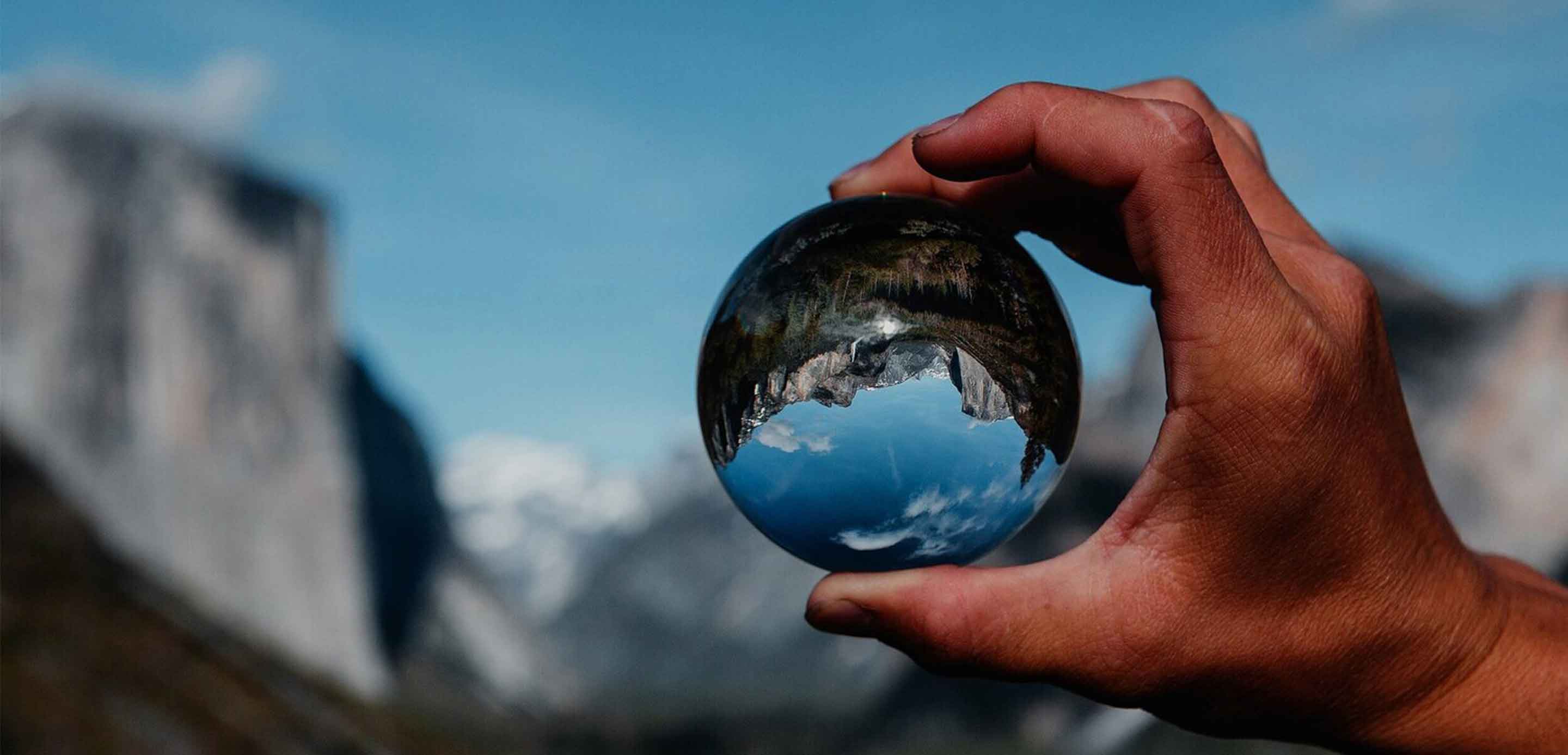 A person holding a glass ball with a mountain in the background, capturing a moment of serenity and wonder.